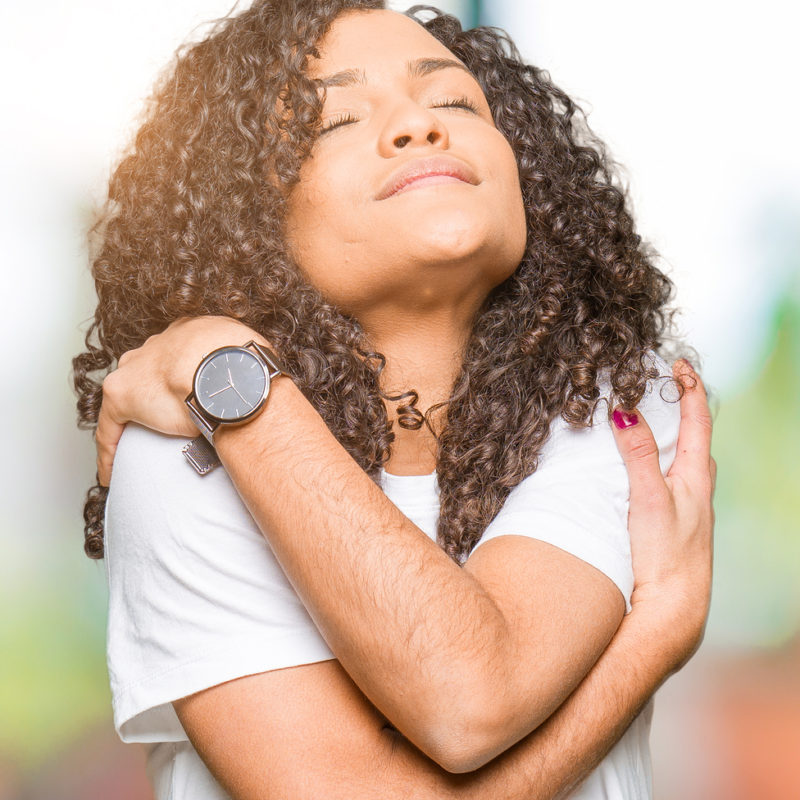Young beautiful woman with curly hair wearing white t-shirt Hugging oneself happy and positive, smiling confident. Self love and self care after trauma therapy St. Petersburg, FL and PTSD Treatment in St. Petersburg, FL 33713 and in Online therapy in Florida