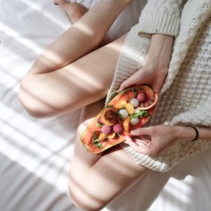 Self-Care of having a healthy snack, woman holding her fruit bowl on bed for self-care as a part of an anxiety therapy in St. Petersburg, FL. Online therapy in Florida is available here with a skilled therapist in St. Pete.