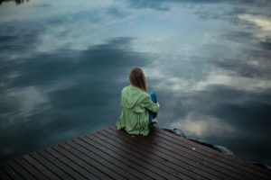 Woman sitting on a dock holding her legs. Anxiety therapy in St. Petersburg, FL can help you via online therapy in Florida for marriage counseling, maternal mental health, relationship therapy and more. 