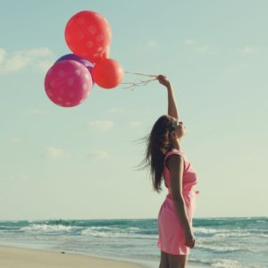 Woman holding red balloons on the beach feels connected to her inner child. You can get help from a counselor in St. Petersburg, FL via online therapy in Florida here!