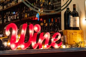 Wine light up sign on a bar with bottles of wine around. Therapy in St. Petersburg, FL can help you cope with anxiety, depression, stress and overwhelm. Get started with online therapy in Florida with a St. Pete therapist here!
